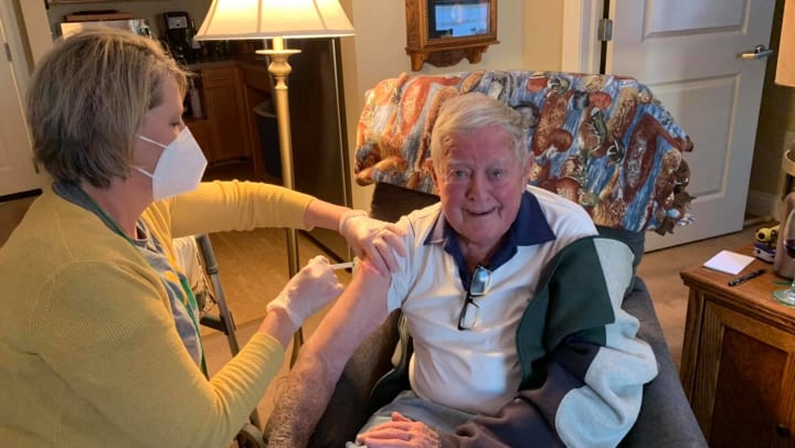 Masked nurse giving a COVID-19 vaccine to a senior man