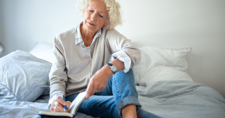 Adult woman on bed writing in journal.