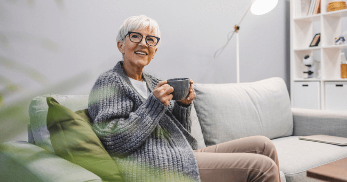 Elder woman with coffee cup in hand sitting on a sofa.