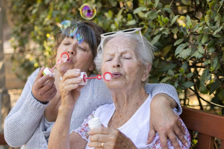 Elderly mother and her daughter blowing soap bubbles for summer fun.