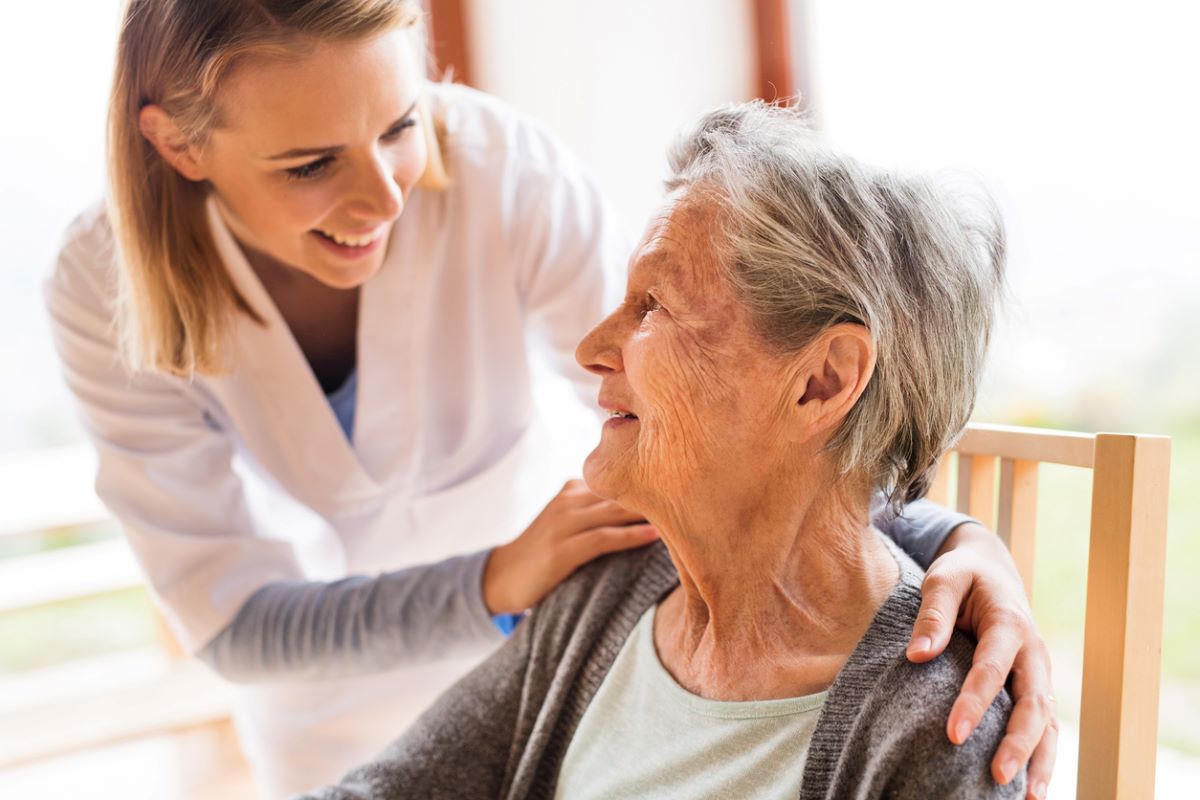 A nurse talking to a senior woman sitting in a chair.